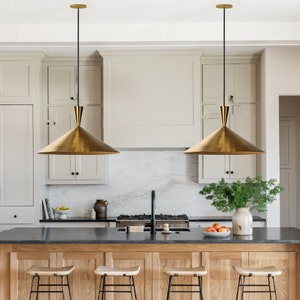 May include: Two gold pendant lights with black cords hang over a kitchen island with a black countertop and wooden cabinets. The lights are shaped like cones and have a modern design.