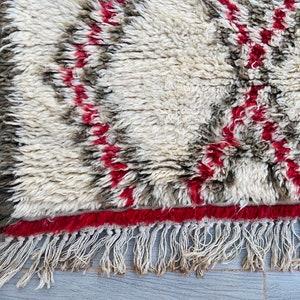 May include: A white, fluffy rug with red and brown stripes and a fringe border.