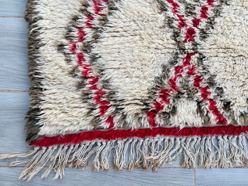May include: A white, fluffy rug with red and brown stripes and a fringe border.