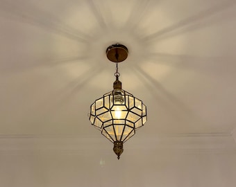 May include: A decorative pendant light with a geometric design. The light fitting has a bronze finish and clear glass panels. The light is on, illuminating the interior. The fixture is suspended from the ceiling.