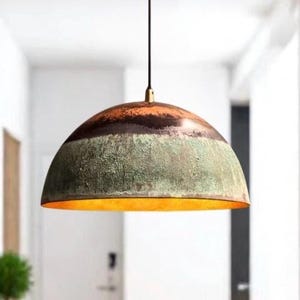 May include: A dome-shaped pendant light fixture with a textured, multi-toned surface. The top section is brown, transitioning to a green-grey middle, and a gold-colored interior. The light hangs from a black cord.