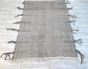 May include: Black and white striped rug with fringe on all sides. The rug has a woven texture and is made of natural fibers.