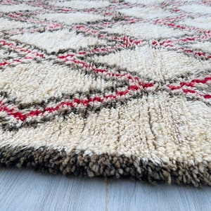 May include: A white, fluffy rug with a geometric pattern of red and gray lines. The rug has a thick pile and is made of wool.