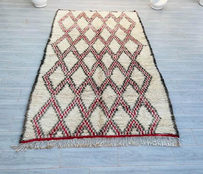 May include: A white and red Moroccan rug with a diamond pattern. The rug has a fringe border.