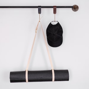 May include: A black yoga mat hanging from a leather strap on a black metal rod. A black baseball cap hangs from a leather strap on the same rod.