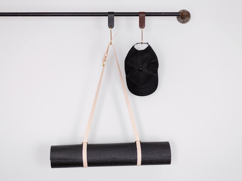 May include: A black yoga mat hanging from a leather strap on a black metal rod. A black baseball cap hangs from a leather strap on the same rod.