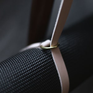 May include: A black yoga mat with a light brown leather strap and a gold metal ring.