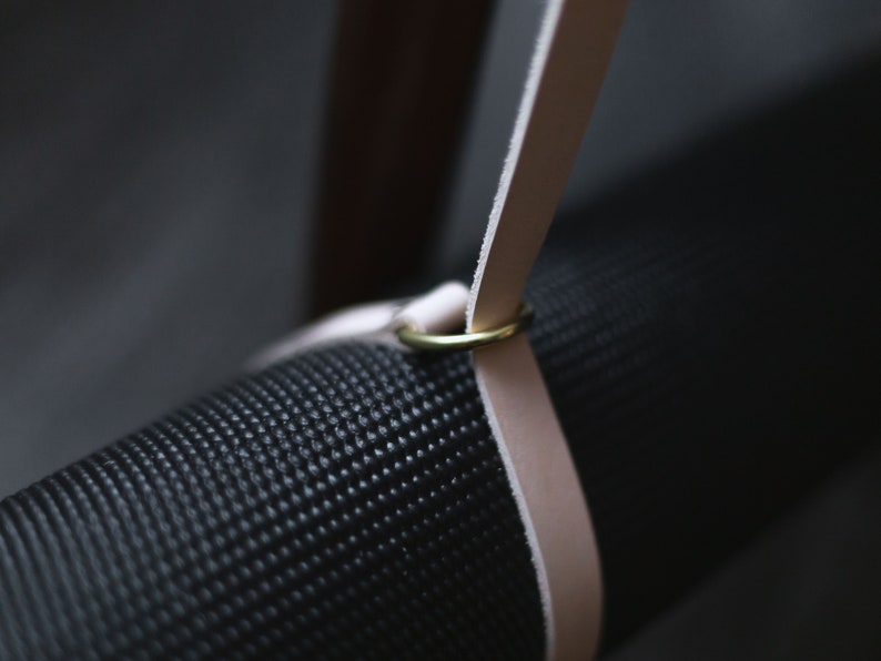 May include: A black yoga mat with a light brown leather strap and a gold metal ring.