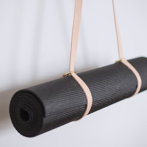 May include: A black yoga mat hanging from a light brown leather strap with brass hardware.