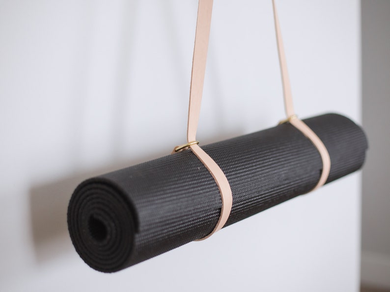 May include: A black yoga mat hanging from a light brown leather strap with brass hardware.