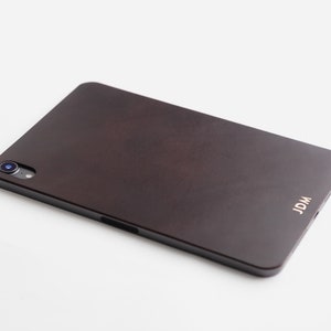 May include: A dark brown leather case for a tablet with a camera lens and the word "JDM" embossed in gold on the back.