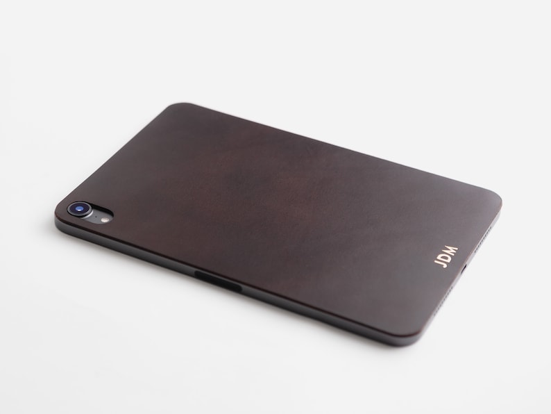 May include: A dark brown leather case for a tablet with a camera lens and the word "JDM" embossed in gold on the back.