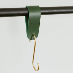 May include: A green leather hook with a brass S-shaped hook hanging from a black metal rod.