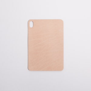 May include: A light brown leather cutting board with a rounded edge and a small hole in the top left corner.