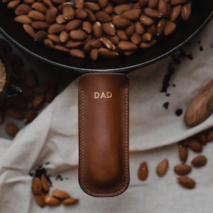 May include: A brown leather pot holder with the word "DAD" embossed in gold lettering.