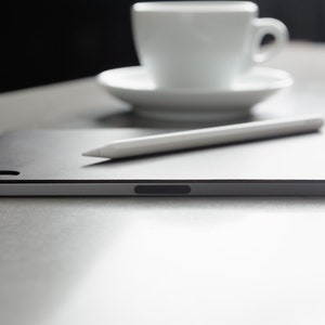 May include: A black tablet computer with a white stylus resting on top. The tablet is on a grey surface.