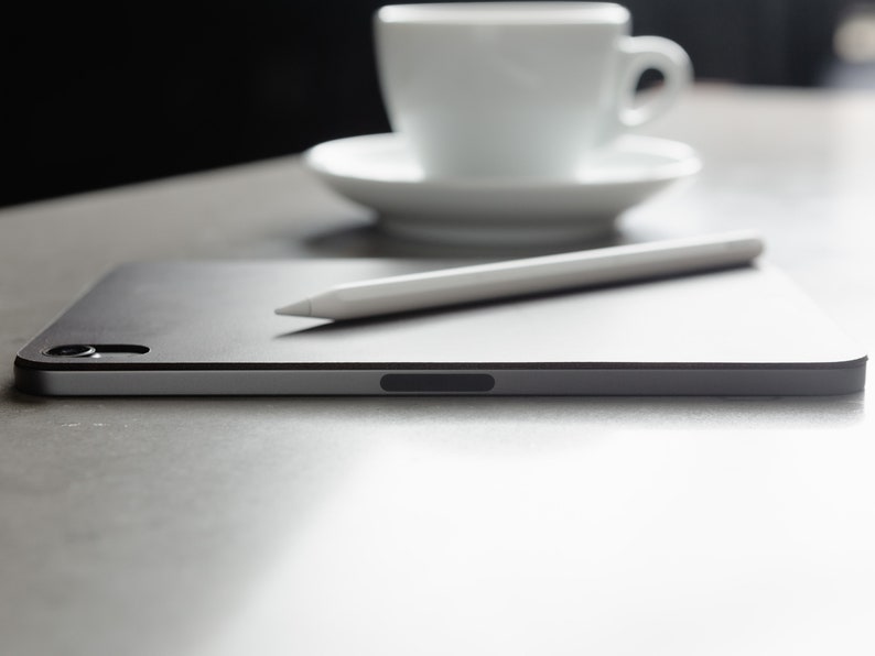 May include: A black tablet computer with a white stylus resting on top. The tablet is on a grey surface.