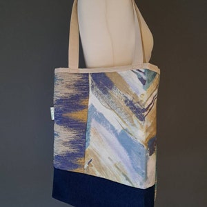 May include: A blue, beige and white patterned tote bag with a navy blue bottom. The bag has two beige straps.