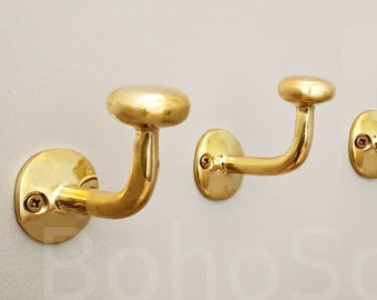 May include: Three gold-toned metal hooks with a mushroom-shaped top. The hooks are mounted on a white wall.