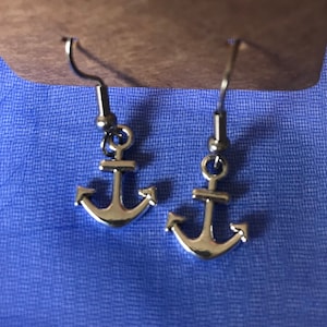 May include: A pair of silver anchor earrings with a simple design. The earrings are on a blue background.