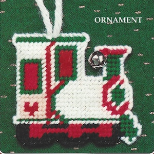 Puede incluir: Un adorno navideño de fieltro blanco, rojo y verde con forma de tren con una campana en la parte superior. El adorno está etiquetado como "ORNAMENT".
