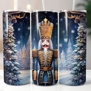 Op de afbeelding: Een hoge, geïsoleerde beker met een feestelijk Notenkraker-ontwerp. Het kunstwerk toont een Notenkraker-soldaat in een blauw uniform met gouden accenten, tegen een besneeuwde winterscène met kerstbomen en een kasteel. De beker bevat een rietje.