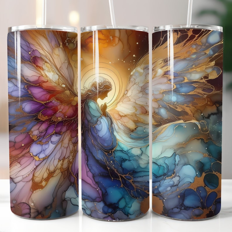 Puede incluir: Un vaso de acero inoxidable con un dise&ntilde;o envolvente que presenta un &aacute;ngel de acuarela con las alas extendidas. El &aacute;ngel es en tonos de azul, morado y dorado, con un halo y una pose de oraci&oacute;n. El fondo tiene un efecto de acuarela.