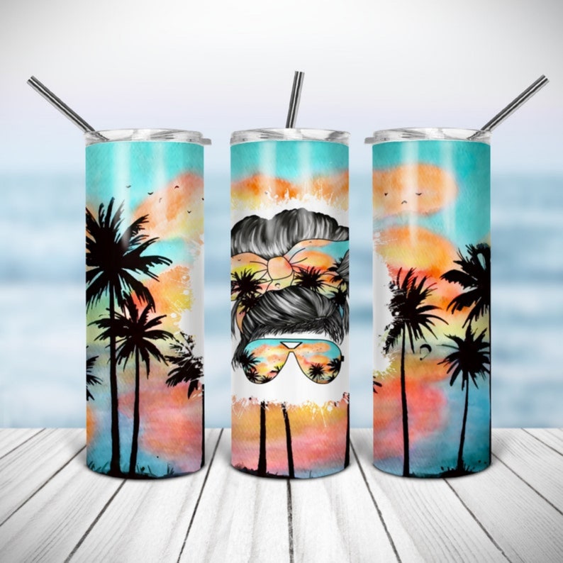 Puede incluir: Un juego de tres vasos aislados de acero inoxidable con un dise&ntilde;o tropical. Cada vaso presenta una escena de puesta de sol con palmeras y la cara de una mujer con gafas de sol. Incluye una pajita plateada.