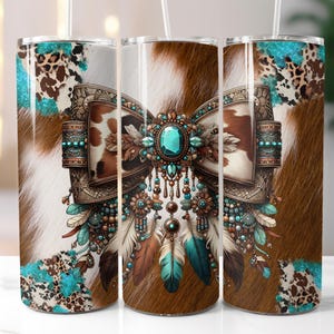 May include: Three stainless steel tumblers with a cowhide pattern and a decorative bow design. The bow features a large turquoise gemstone, feathers, and turquoise beads. The tumblers have a white straw.