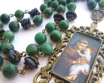 May include: A green and black rosary necklace with a bronze pendant featuring a picture of Saint Anthony of Padua holding a baby.