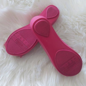 May include: A pair of pink rubber ballet flats with the brand name "Melissa" printed on the soles.