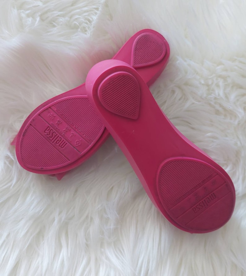 May include: A pair of pink rubber ballet flats with the brand name "Melissa" printed on the soles.
