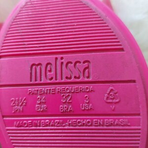 May include: Pink Melissa brand shoe sole with size information in Japanese, European, Brazilian, and US sizing. The text reads "Patente Requerida" and "Made in Brazil Hecho en Brasil".