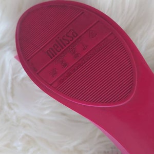 May include: Close-up of the bottom of a pink Melissa brand shoe. The shoe has a textured sole and the words "Melissa" and "Made in Brazil" are printed on the sole.