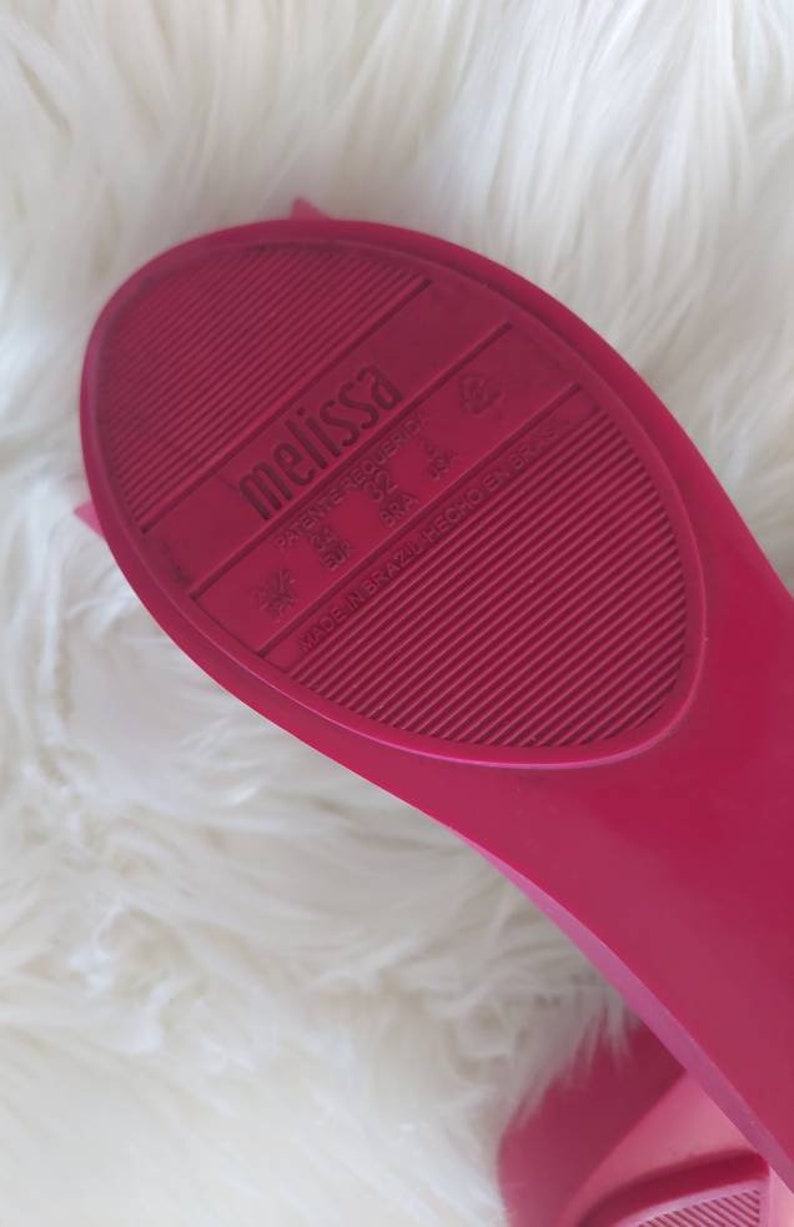 May include: Close-up of the bottom of a pink Melissa brand shoe. The shoe has a textured sole and the words "Melissa" and "Made in Brazil" are printed on the sole.