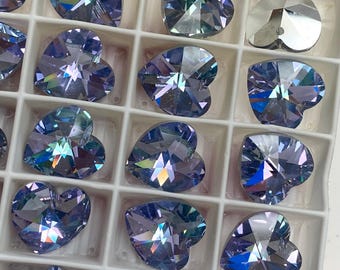 May include: Close-up of heart-shaped, faceted crystals in shades of blue and purple. The crystals are arranged in a grid pattern within a white tray, showcasing their reflective surfaces and intricate cuts. These decorative crystals are ideal for crafts.
