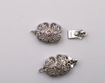 May include: Two silver-toned metal clasps with ornate designs and clear rhinestones. The clasps are oval-shaped and have a filigree pattern.
