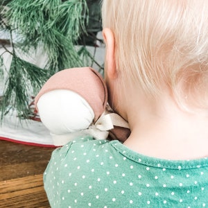 May include: A young child with blonde hair wearing a green shirt with white polka dots holds a pink and white fabric doll.