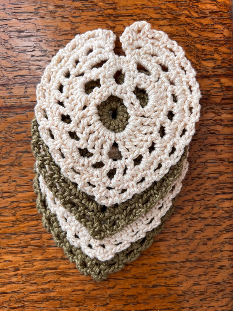 May include: Four crocheted coasters, two in a light beige color and two in a dark olive green color. The coasters are stacked on top of each other, with the beige coasters on top.