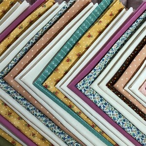 May include: A stack of fabric squares in various colors and patterns, including floral, polka dot, and solid colors. The fabric squares are arranged in a diagonal pattern.