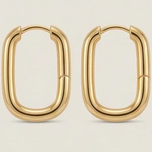 Könnte beinhalten: Ein Paar goldfarbene, rechteckige Creolen. Die Ohrringe haben eine glatte, polierte Oberfläche und einen Klappverschluss. Das Design ist ein einfacher, moderner Stil.