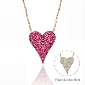 May include: A gold-toned necklace featuring a heart-shaped pendant encrusted with pink gemstones. The pendant is suspended from a delicate chain. A smaller image shows the pendant's reversible design.