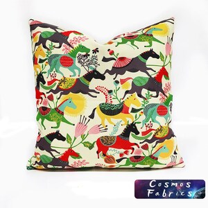 May include: A colorful throw pillow with a pattern of horses and flowers. The horses are in various colors, including red, yellow, green, and blue. The flowers are pink and white. The background is a cream color.