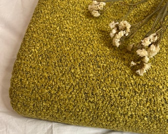 May include: A close-up of a yellow textured fabric with a sprig of dried white flowers on top.
