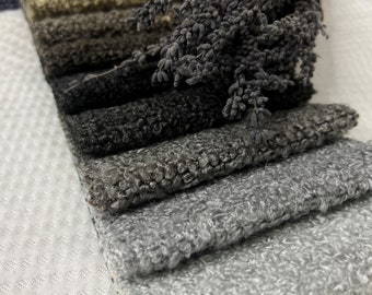 May include: A stack of fabric swatches in various shades of gray, from light to dark, with a sprig of dried lavender flowers on top.