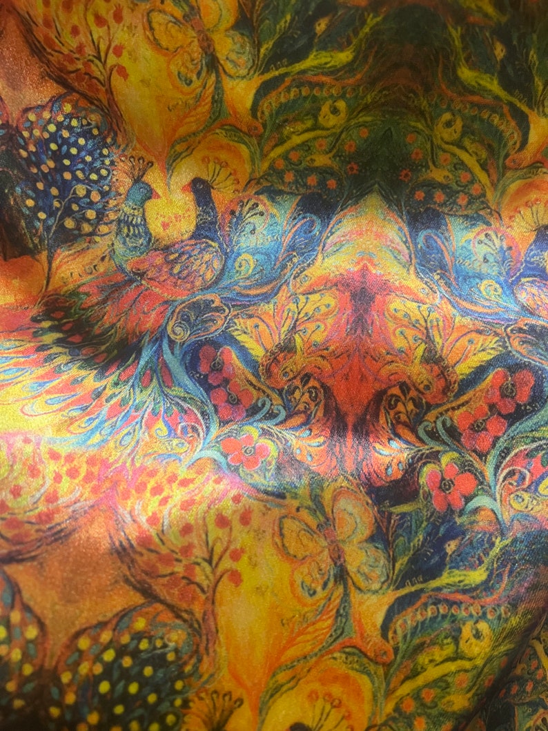 Op de afbeelding: Een kleurrijke stof met een pauwenmotief. De stof heeft een herhalend patroon van pauwen, bloemen en vlinders in tinten blauw, groen, geel, oranje en rood.