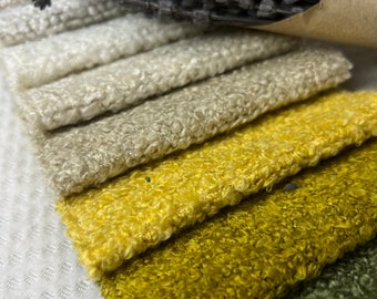 Op de afbeelding: Een close-up van een stapel stofstalen in verschillende tinten beige, geel en groen. De stof heeft een pluche textuur.