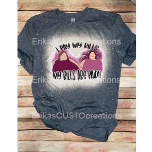 Może przedstawiać: Szary T-shirt z wzorem rozpryskanym wybielaczem, przedstawiający dwie kreskówkowe kobiety i tekst "Płacę rachunki, moje rachunki są opłacone!"