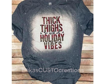 Puede incluir: Una camiseta gris con un diseño blanqueado que dice "Thick Thighs and Holiday Vibes" en letras rojas, negras y blancas con un fondo de estampado de leopardo.