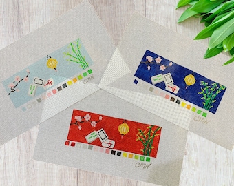May include: Three needlepoint canvases with different colored backgrounds. Each canvas features a design of a red lantern, bamboo, and cherry blossoms. The canvases are labeled with the colors used in the design.